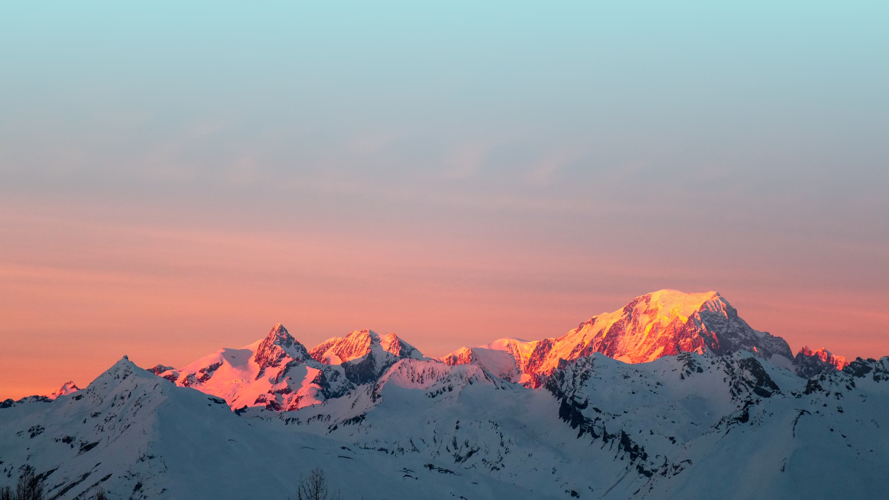 A mountain range with a sunrise, coming from behind the camera, reflecting off them.